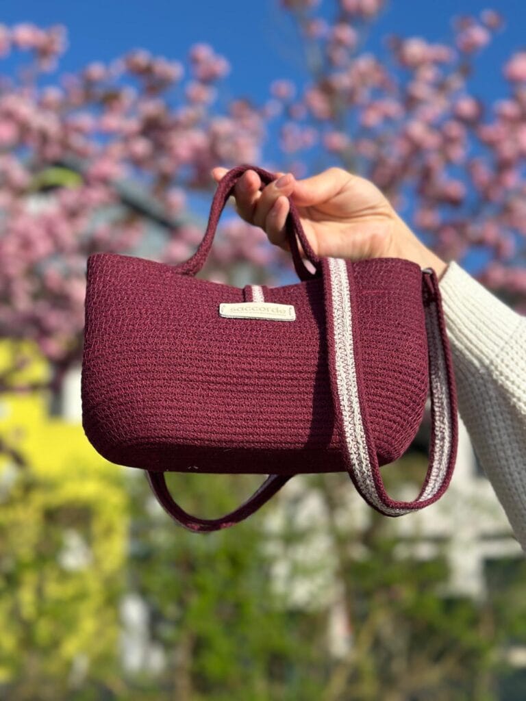 Mini sac en corde couleur vin Lovène porté à la main, fond floral